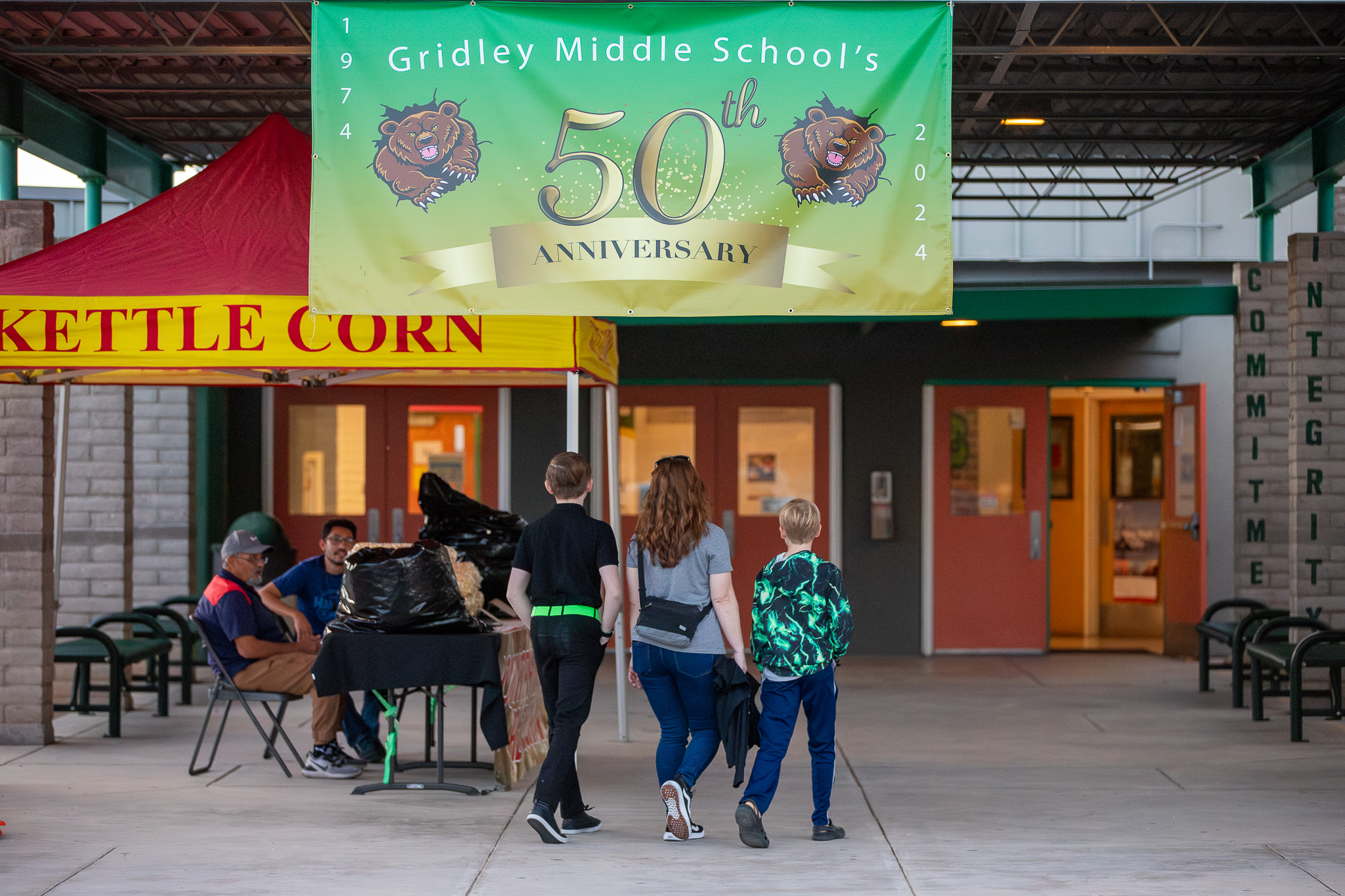 A family walks into the school under the 50th Anniversary banner and next to the Kettle Corn tent