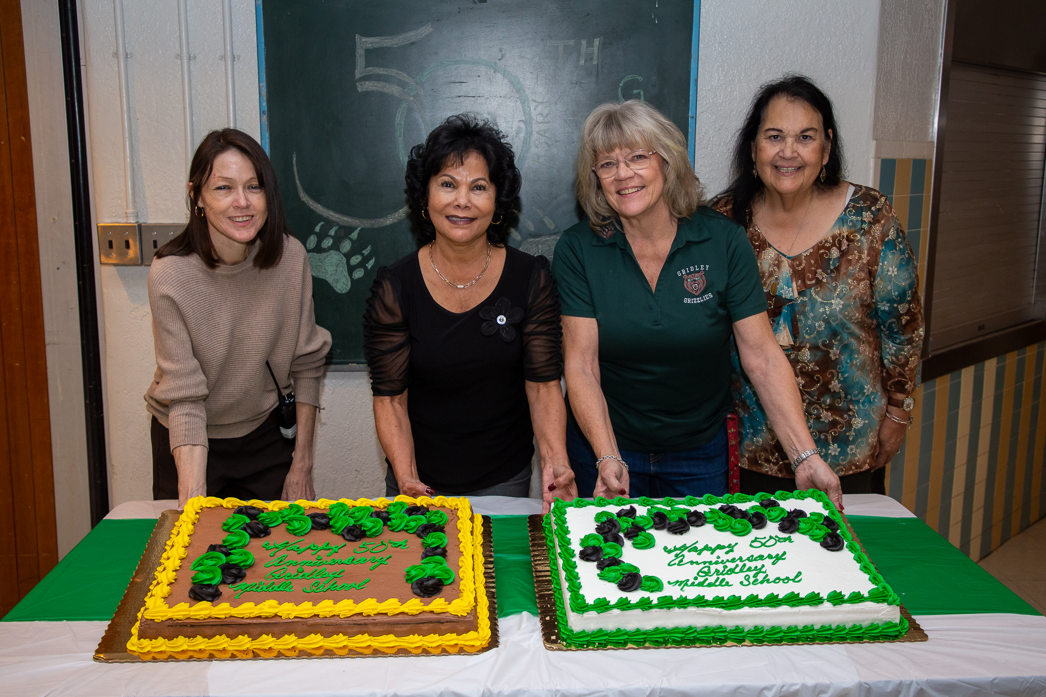 Four women smile with two sheet cakes to celebrate Gridley's anniversary