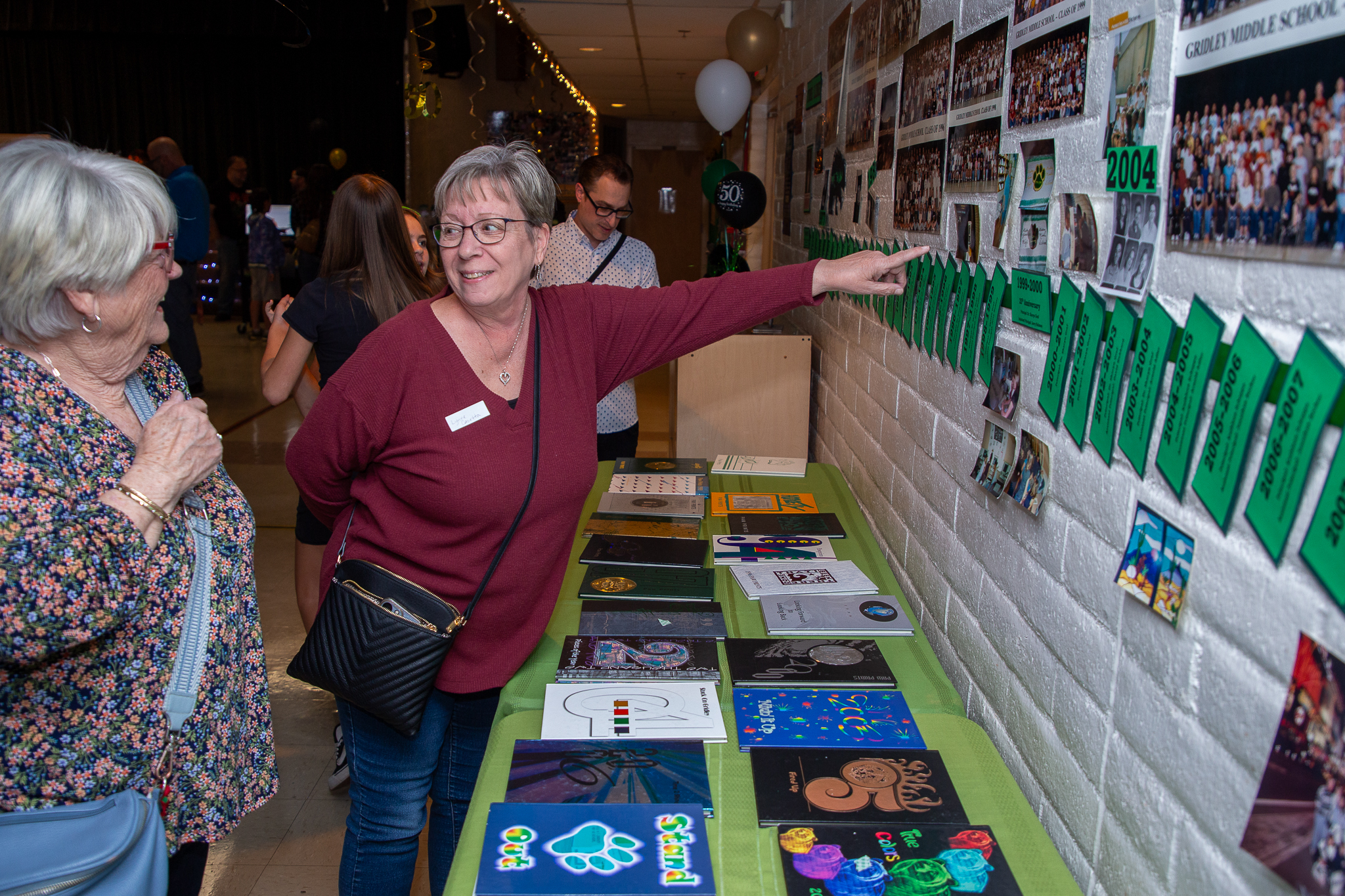 A woman points to a photo on the wall as another woman smiles