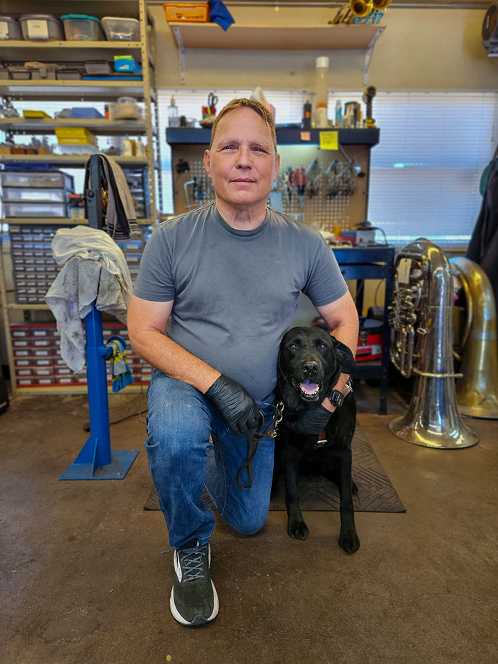 A man poses with his guide dog in the music instrument repair shop