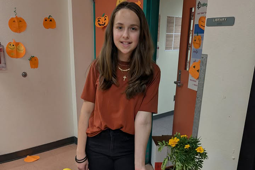 A girl in an orange shirt smiles, with pumpkin decorations around her