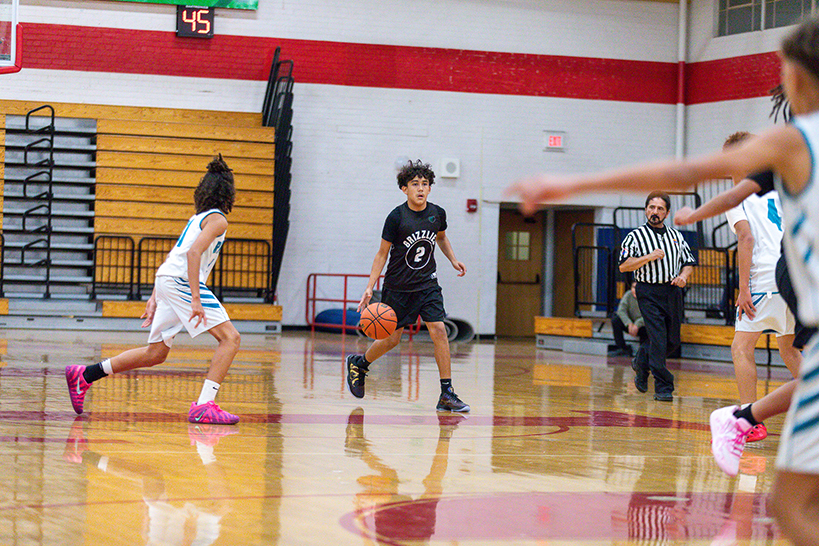 A boy dribbles the ball down the court past his opponents