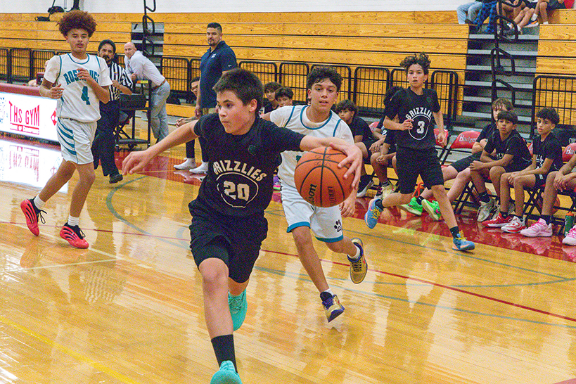 A boy dribbles the basketball as he runs away from his opponents