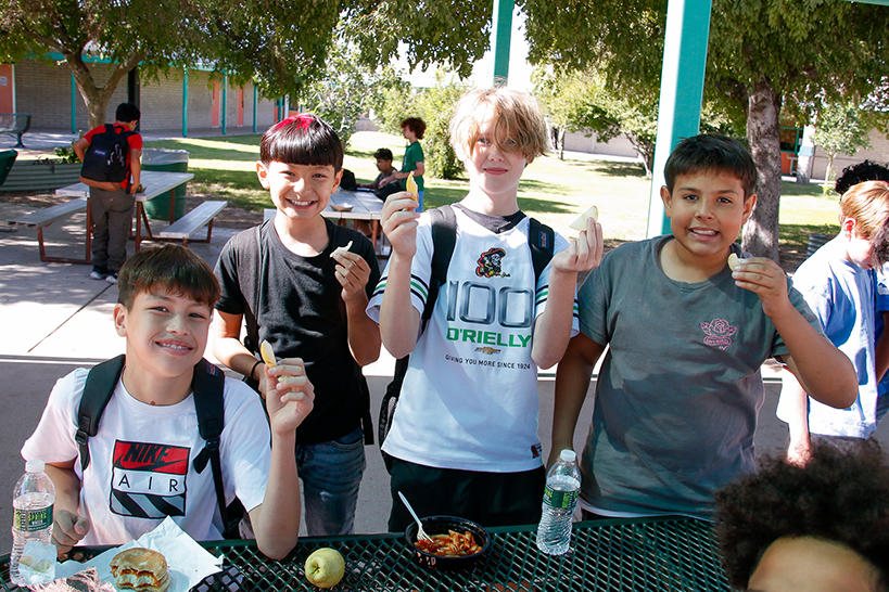 Four preteen boys hold up pear slices during lunch outside