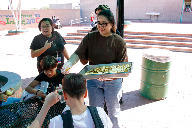 A woman with glasses hands out pear slices to students