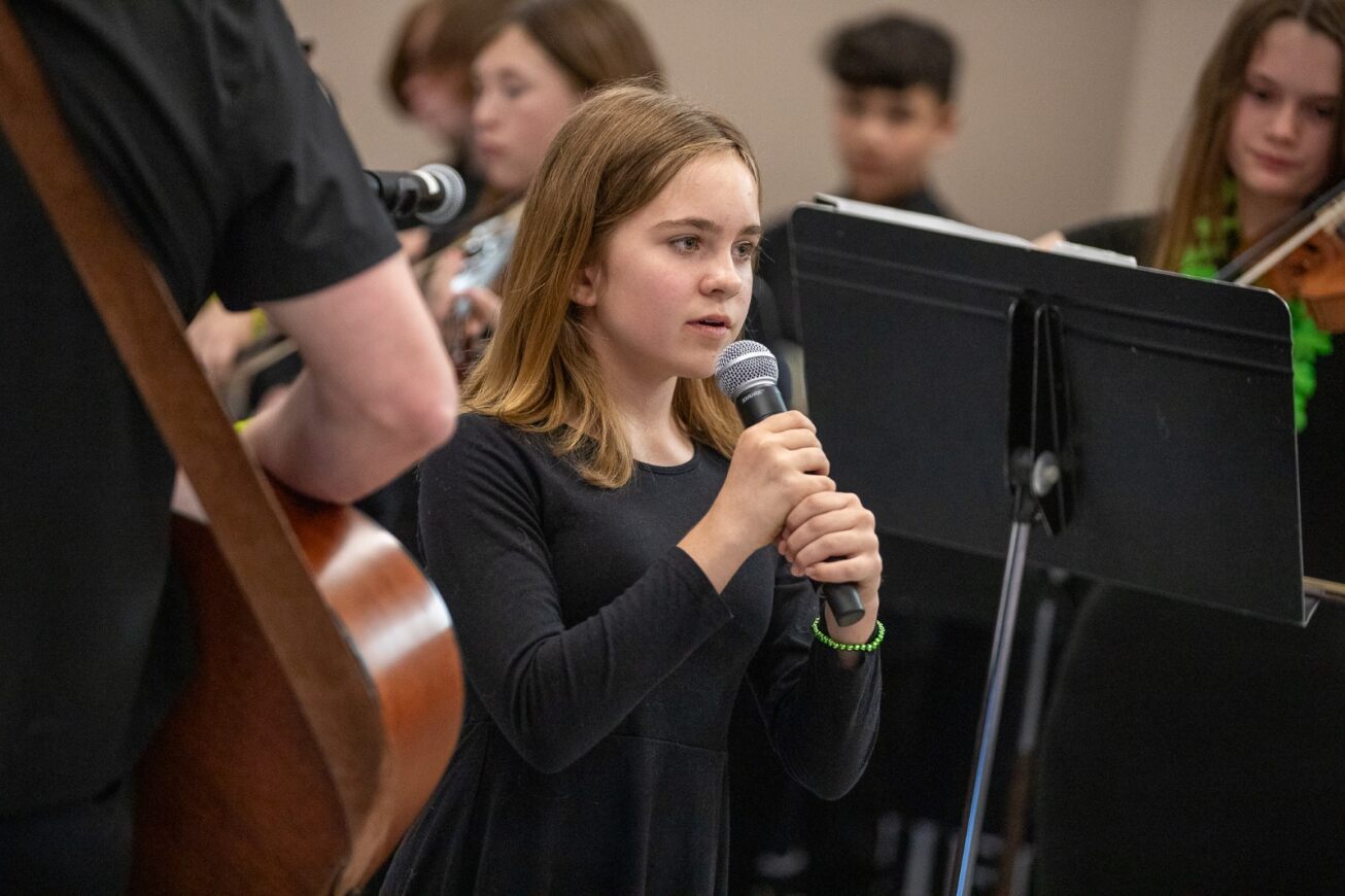 A girl with short blonde hair performs a solo at the Governing Board meeting