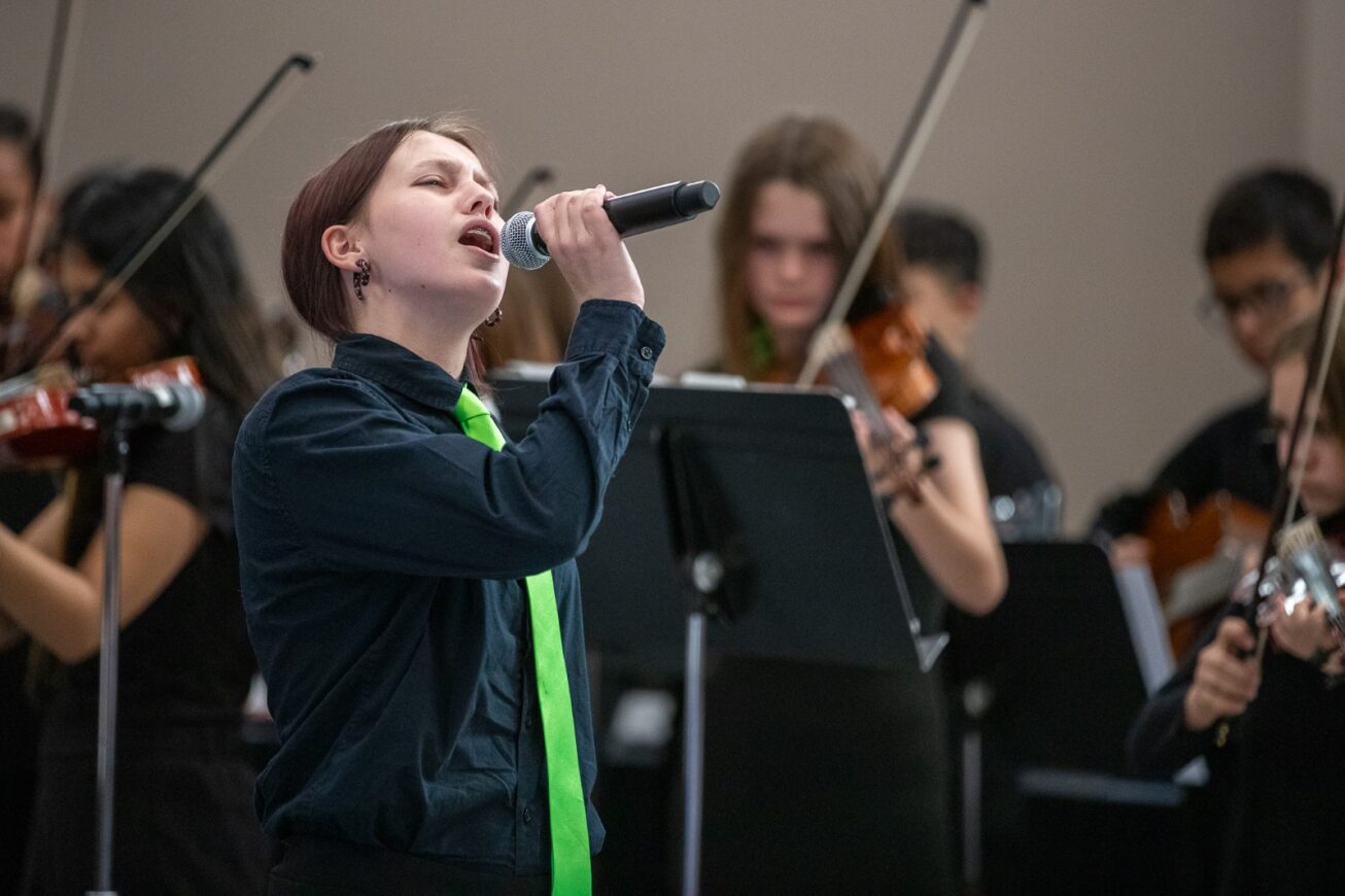 A Gridley student in a black shirt and lime green tie sings a solo at the Governing Board meeting